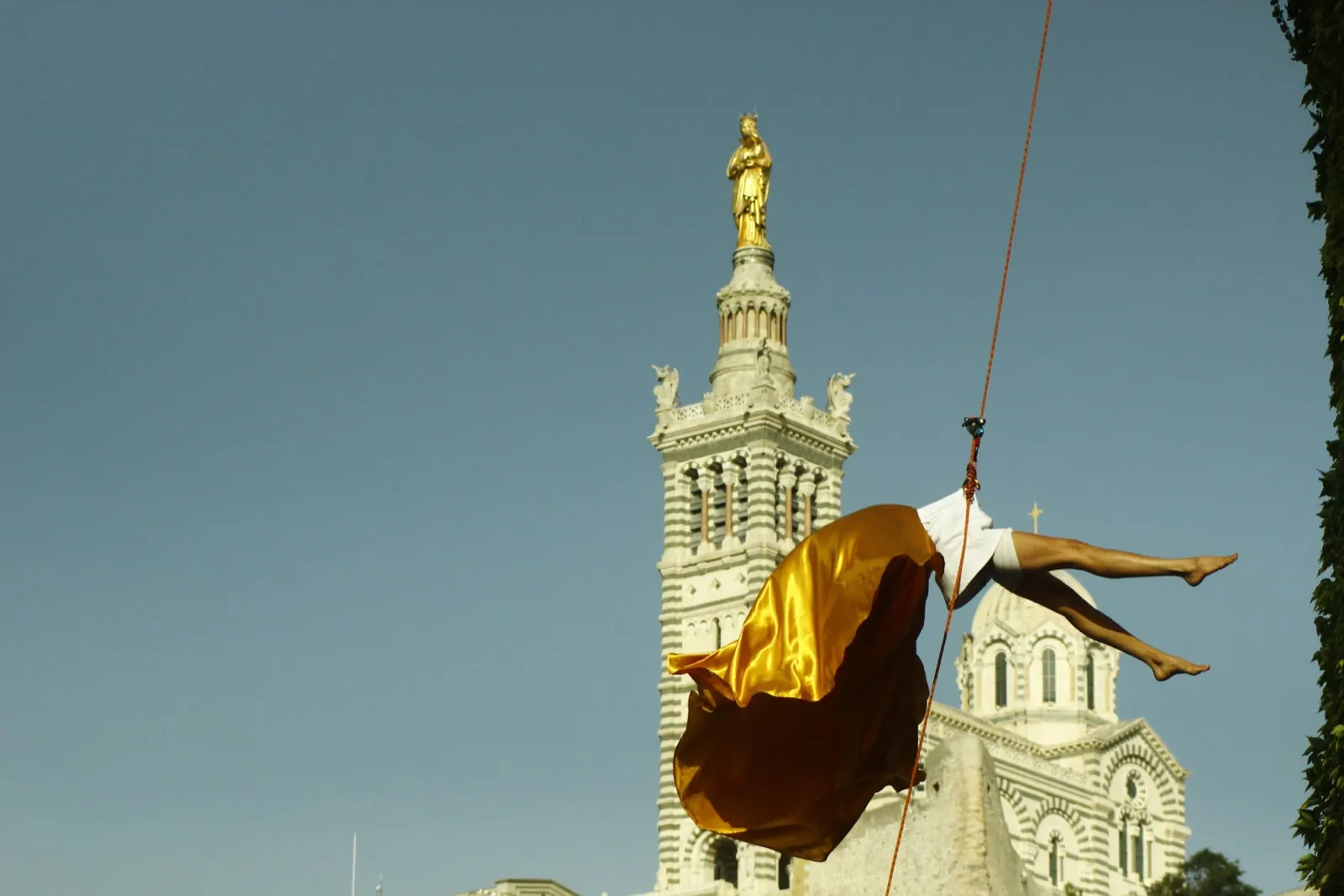 A dancer in gold fabric hanging below the tower of Notre-Dame de la Garde